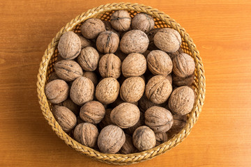 Walnuts in a wooden round bowl on a wooden table in soft focus, top view or flat lay of healthy vegan food, brown monochrome photo