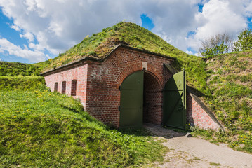 Fototapeta na wymiar Bunker covered with ground and grass, dugout made by bricks and steel hidden under hill.