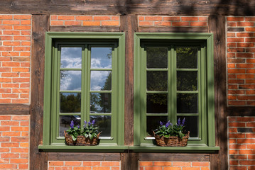 Windows with green frames and decorated by flowers in baskets, .surrounded by bricks wall.