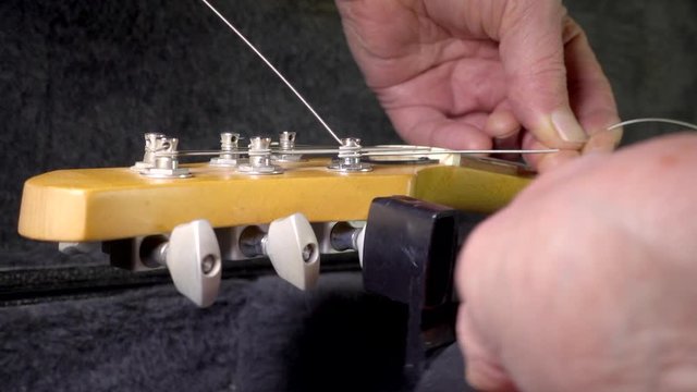 Slow motion close POV shot of hands with a newly fitted string on an electric guitar, using a string winder tool on a tuning peg to tighten.