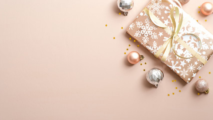 Christmas banner. Top view gift box wrapped festive pink paper, balls, confetti over beige background with copy space. Merry Christmas greeting card mockup, New Year postcard template.