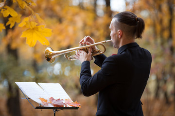 young slender jazz trumpeter in black jacjet or suit plays autumn melody or song with notes on...