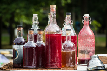 group of different shaped transparent bottles with red and burgundy beverages for cocktails at the outdoor summer party in park