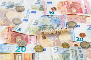 Steuern Schriftzug über Euro Geldscheinen und Münzen, Nahaufnahme