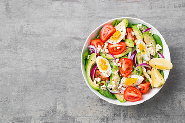 Fresh avocado salad with tomato,cucumber , boiled eggs and spinach served with lemon and ricotta cheese. Top view.