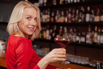Cheerful beautiful woman in red dress celebrating at the bar, having delicious cocktail, copy space