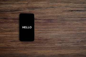 Turned on black phone displaying hello on wood desk background.