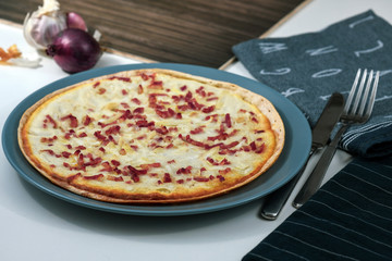 Taditional food `Tarte Flambee` or `Flammkuchen` from German-French Alsace border region. The name means `pie baked in the flames`, similar to a thin pizza with bacon and soured cream