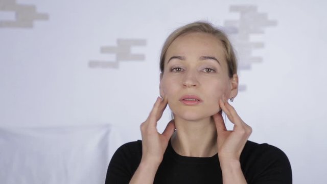 blonde woman doing self-massage, anti-aging facial massage in office. daily face fitness and face building.