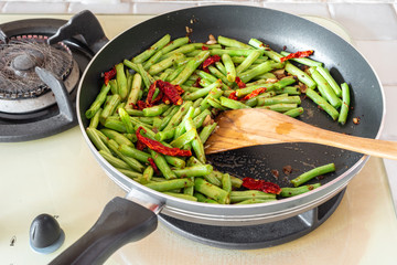 Home cooked food. French green beans, dried chillies and garlic in stir-fry pan on cooking stove