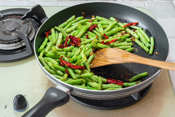 Home cooked food. French green beans, dried chillies and garlic in stir-fry pan on cooking stove