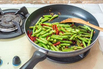 Home cooked food. French green beans, dried chillies and garlic in stir-fry pan on cooking stove