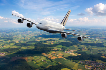 White aircraft in flight. The passenger plane flies high over the green plain. Front view of airplane.