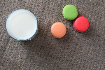 Macarons three pieces red, green, orange scattered and glass with milk on burlap tablecloth. Top view.