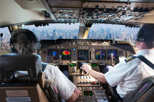 The cockpit of a modern passenger aircraft in flight. Pilots at work. A view from the cockpit to the skyscrapers of the business center of a huge city.