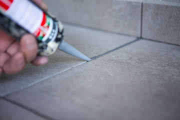 The hand of a construction worker filling the gap between ceramic tiles with silicone