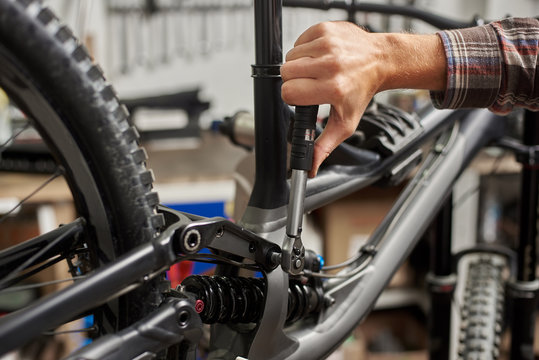 Cropped shot of man mechanic working in bicycle repair shop, worker repairing mountain bike using special tool