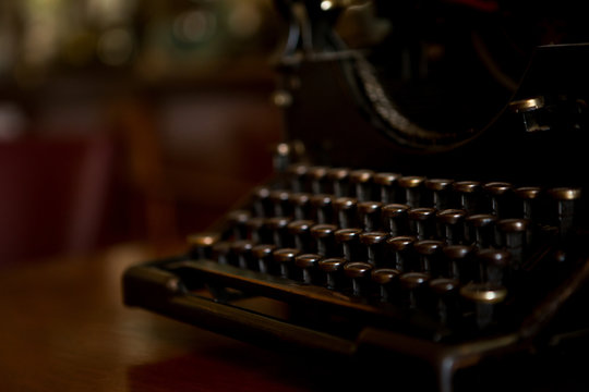 Selective focus on the keyboard key on an old black rustic typewriter on a desk in the office. The typewriter is a lot old so the letters on the keys are almost worn out. Copy space.