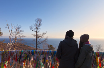 Baikal Lake. Listvyanka. Tourists admire the sunset over lake and the sourceof the  Angara River from a gazebo with colored ribbons on the rock of the Chersky Stone © Katvic