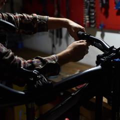 Cropped shot of male repairman working in bicycle repair shop, mechanic repairing bike using special equipment, wearing protective gloves
