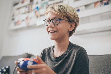 Boy sitting on sofa, playing with game console online with friends. Teen on the couch makes grimace while engaged with a video game. Addicted gamer enjoy the challenge. Addiction, dependence concept.