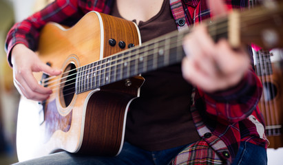 Close-up girl is playing acoustic guitar. Focus on body of guitar