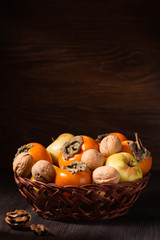 Obraz na płótnie Canvas Autumn fruits and nuts in a basket, wooden background. Copy space. Fall food still life with persimmon, walnuts, apples, rustic style