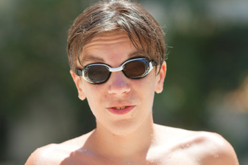 Portrait of handsome teenager boy wearing black goggles in swimming pool outdoors in a sunny summer day