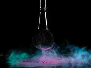 Professional cosmetic brush, pink and turquoise powder explosion on black background