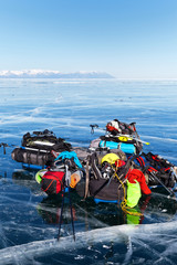 Obraz premium Baikal Lake. A pile of tourist equipment: tents, backpacks, mats, protective helmets, skates on beautiful blue ice against the boundless ice expanses of the frozen lake. Winter tourism concept