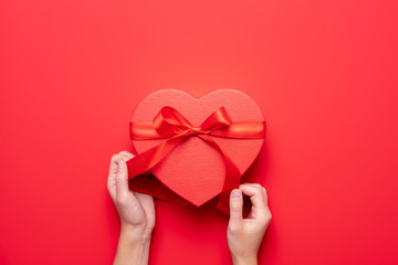 Female hands holding red heart gift box on red background. Valentine's Day composition