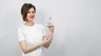 pretty woman doctor with dark hair in protection gloves pushes and shakes syringe standing against white wall close view copy space