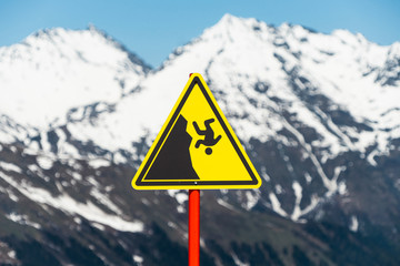 Yellow danger sign in the mountains. Hiking Safety Warning. Caution of falling from the Mountain.
