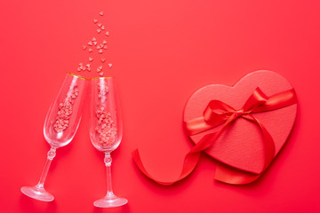 Two champagne glasses with splash of red heart shaped confetti on red background. Top view, flat lay, copy space. Valentine's Day concept