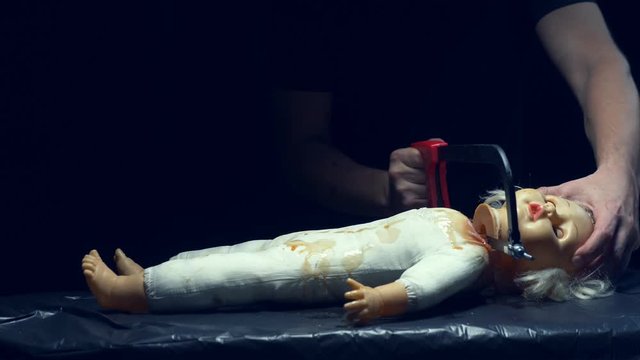 male hands saw off a scary dolls head, halloween