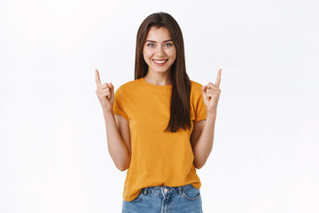 Pleased, happy and friendly-looking young brunette woman in yellow t-shirt, raising fingers and...