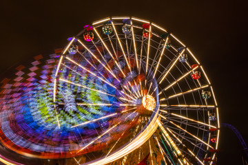 Two rides in motion in amusement park, night illumination. Long exposure.