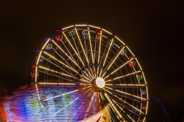 Two rides in motion in amusement park, night illumination. Long exposure.