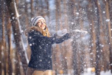 Happy young woman plays with a snow in sunny winter day. Girl enjoys winter, frosty day.  Playing with snow on winter holidays, a woman throws white, loose snow into the air. Walk in winter forest.