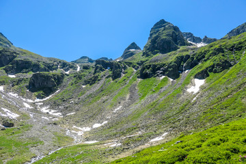 A panoramic view on Schladming Alps, partially still covered with snow. Spring slowly reaching the tallest parts of the mountains. Sharp peaks, slopes partially overgrown with lush green plants.