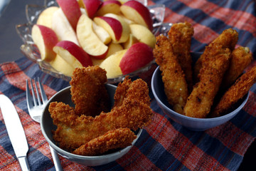 Freshly cooked crispy chicken and fish strips and bowl of sliced apple and pear