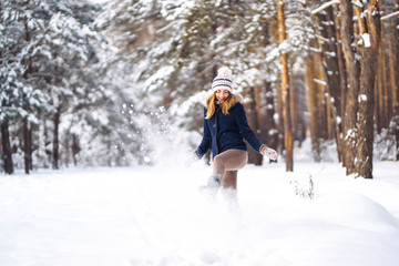 Fototapeta na wymiar Happy young woman plays with a snow in sunny winter day. Girl enjoys winter, frosty day. Playing with snow on winter holidays, a woman throws white, loose snow into the air. Walk in winter forest.