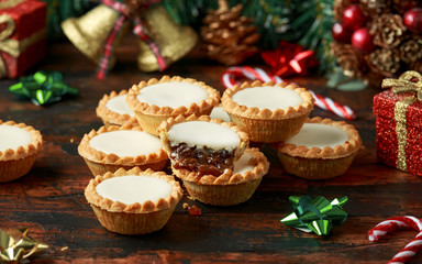 British Christmas iced mince pies with decoration, gifts, green tree branch on wooden rustic table