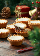 British Christmas iced mince pies with decoration, gifts, green tree branch on wooden rustic table