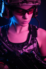 the girl in military overalls airsoft posing with a gun in his hands on a dark background in the haze in neon light