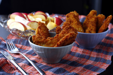 Freshly cooked crispy chicken and fish strips and bowl of sliced apple and pear