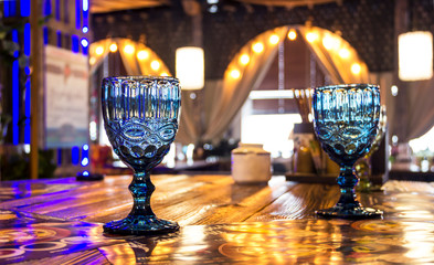 two empty fluted glasses on a leg, stand on a table in a restaurant, with a beautiful decor in a soft yellow setting