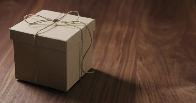 Slow motion man hand bring brown paper gift box on walnut table