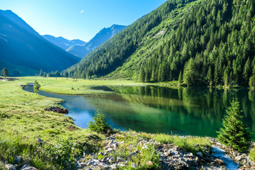 Naklejka na ściany i meble A calm alpine lake. The lake is surrounded with tall mountains. The surface of the lake is calm, it reflects the mountains and sky. Clear and sunny day. Schladming region, Austria