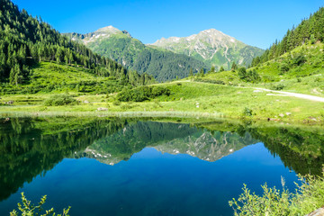 A calm alpine lake. The lake is surrounded with tall mountains. The surface of the lake is calm, it reflects the mountains and sky. Clear and sunny day. Schladming region, Austria
